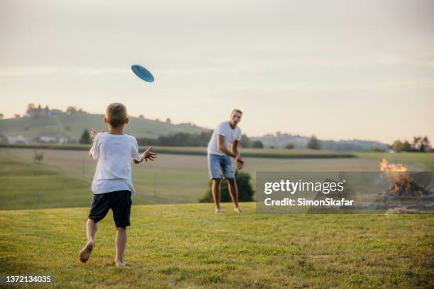 padre juega frisbee con su hijo en el campo durante una fogata en el verano - frisbee fotografías e imágenes de stock