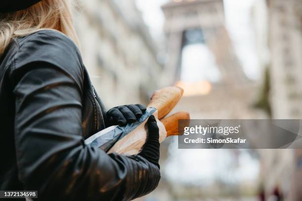 nahaufnahme einer frau, die mit ihren beiden händen baguettes hält, eiffelturm, paris im hintergrund - french baguette stock-fotos und bilder