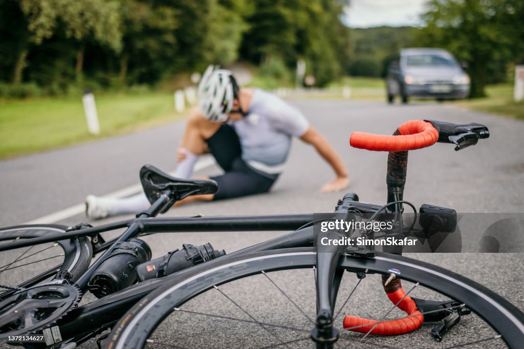 Ciclista herido sentado con dolor junto a la bicicleta de carreras