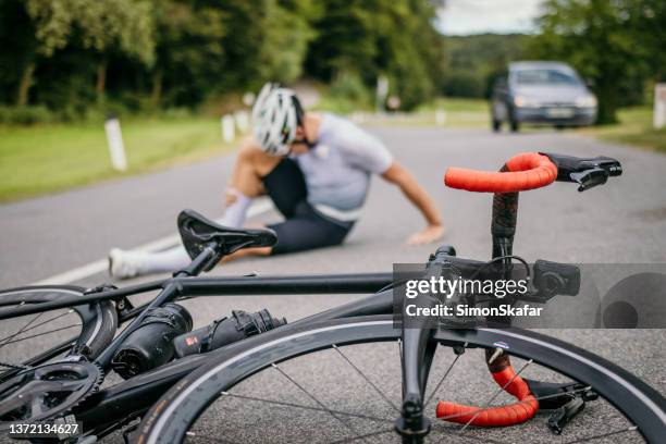 injured cyclist sitting in pain next to the racing bicycle - collide stockfoto's en -beelden