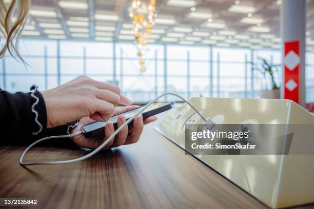 gros plan d’un oman utilisant son téléphone tout en le chargeant sur une station de charge dans un terminal d’aéroport - prise électrique photos et images de collection