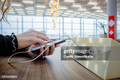 Close-up of a oman using her phone while charging it on a charging station in an airport terminal Close-up of a oman using her phone while charging it on a charging station in an airport terminal
