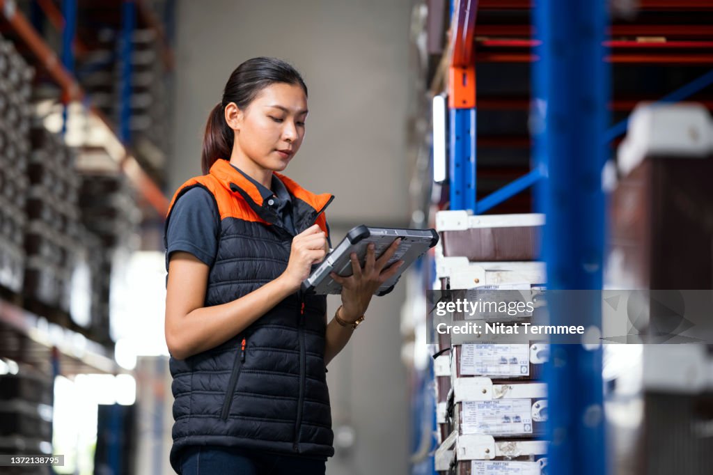 Using Cloud-Based Inventory Management and Tracking System. Female Manager using digital tablet in a factory warehouse while checking and tracking inventory real time data in ERP Software.