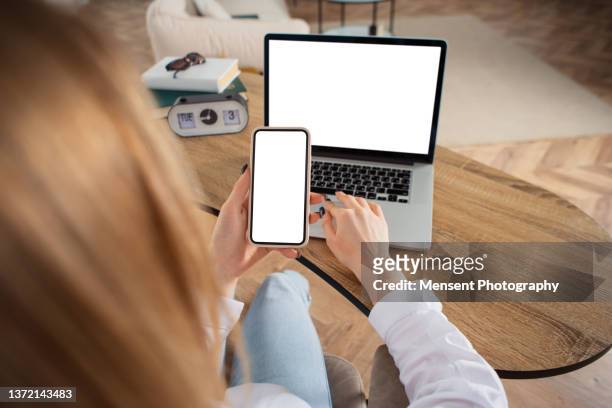 woman sitting a table at home and using a smart phone mockup with white screen - laptop and iphone mockup stock pictures, royalty-free photos & images