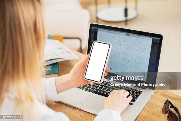 woman sitting a table at home and using a smart phone mockup with white screen - laptop and iphone mockup stock pictures, royalty-free photos & images