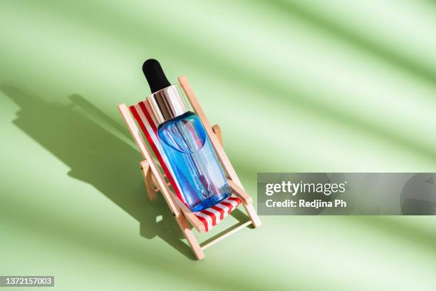bottle of sunburn oil or serum, moisturizer, sunscreen in a mini toy sunbed on green background with  shadow from palm leaves. - tanning bed stock pictures, royalty-free photos & images
