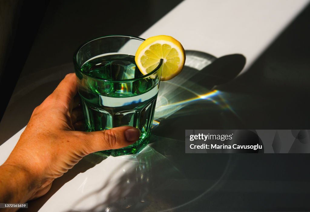 Glass of water with lemon. Sunlight, shadows and reflections.