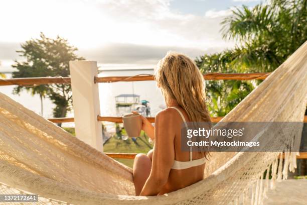 woman relaxing in an hammock on her balcony, she enjoys a cup of coffee - sea cup stock pictures, royalty-free photos & images