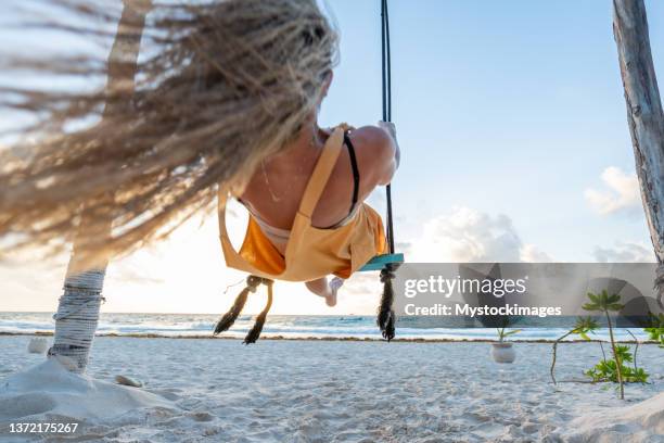 young woman having fun swinging on the beach at sunrise - woman on swing stock pictures, royalty-free photos & images