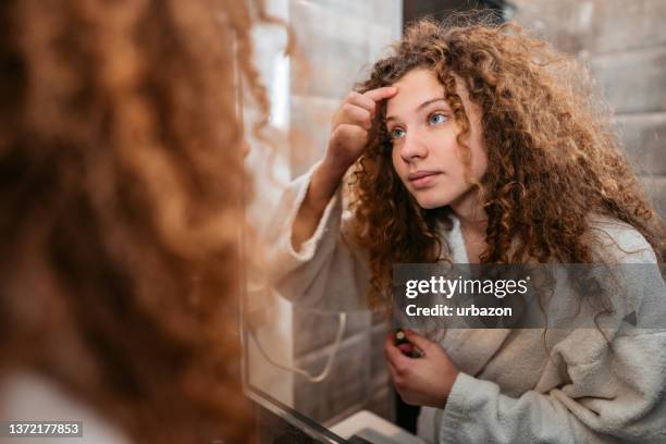 young woman popping a pimple in the bathroom mirror - acne stock pictures, royalty-free photos & images