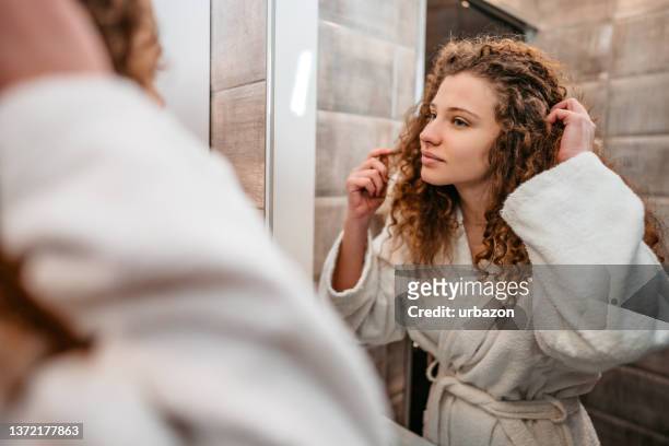 浴室の鏡で自分を見ている若い女性 - curly hair ストックフォトと画像