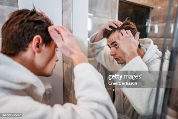 young man looking at himself in the bathroom mirror - men hair stock pictures, royalty-free photos & images