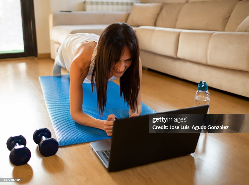 Happy sportswoman doing plank near laptop