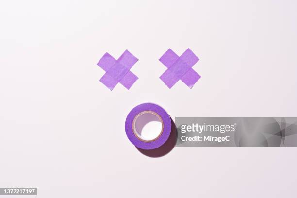 anthropomorphic dizzy face with crossed-out eyes made of purple adhesive tape - surprise emoji stock pictures, royalty-free photos & images