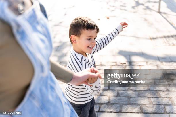 child holding his mother's hand as they cross the street on the pedestrian striping. - cross road children stock-fotos und bilder