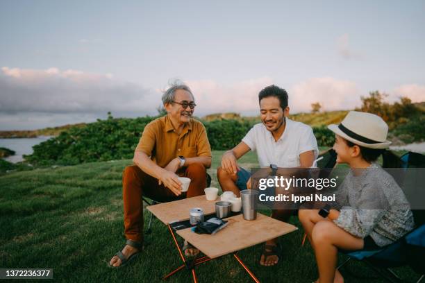 three generation family having fun at campsite by the sea at dusk - asian family camping stock pictures, royalty-free photos & images