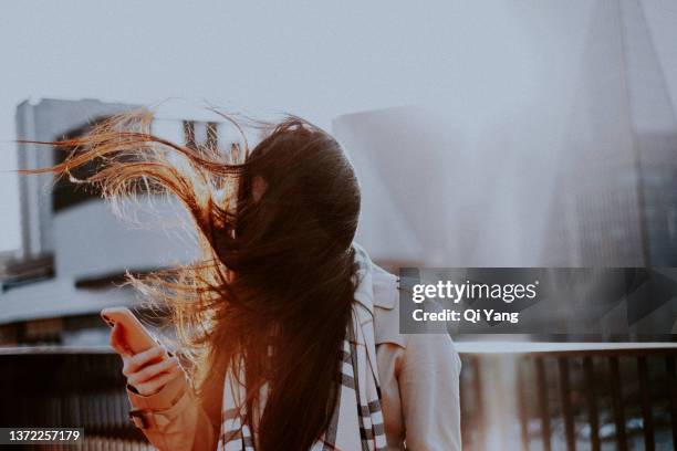 young asian woman using smartphone in morning sunlight, shanghai, china - faces aftermath of storm eleanor stockfoto's en -beelden