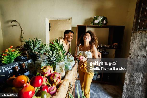 medium wide shot of couple laughing while shopping for fruit in shop during vacation - grocery store produce stock pictures, royalty-free photos & images