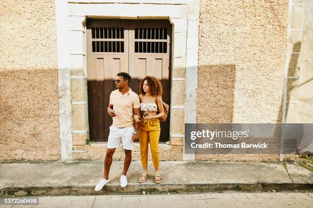 wide shot of couple holding smart phones and standing curbside while waiting for ride during vacation - rinnsteinkante stock-fotos und bilder