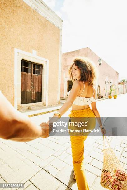 wide shot of smiling woman leading boyfriend by hand while exploring town during vacation - walking personal perspective stock pictures, royalty-free photos & images