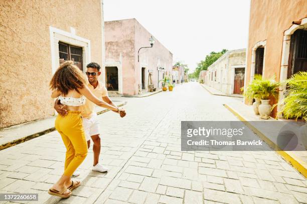 wide shot of smiling couple dancing in street while exploring town during vacation - turismo vacaciones fotografías e imágenes de stock