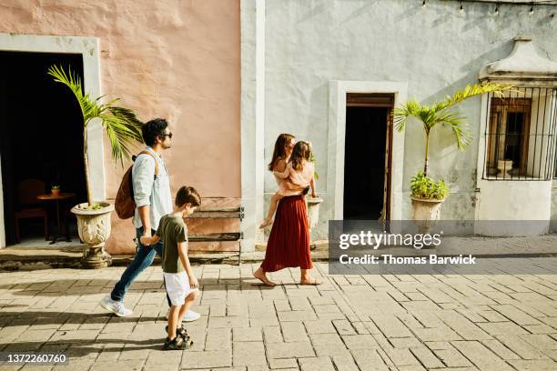 wide shot of family walking down street while exploring town during vacation - town foto e immagini stock