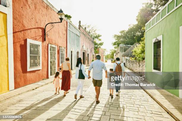 Wide shot rear view of multigenerational family holding hands while exploring town during vacation