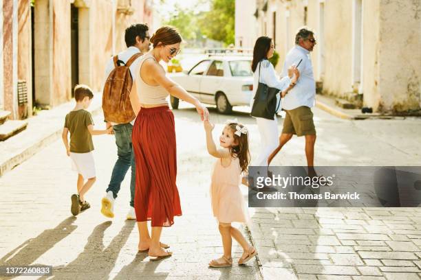 wide shot of smiling mother dancing with daughter while exploring town with family during vacation - discovery bags walking stock-fotos und bilder