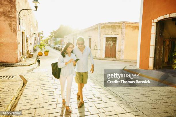 Wide shot of senior couple looking at smart phone while walking through historical town while on vacation