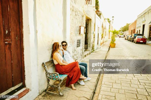 wide shot of smiling couple relaxing on bench while exploring historical town during vacation - mexico tourism stock pictures, royalty-free photos & images