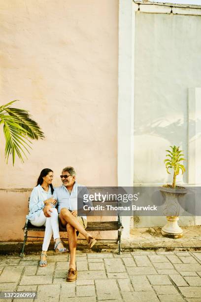 Wide shot of smiling senior couple relaxing on bench while exploring historical town during vacation