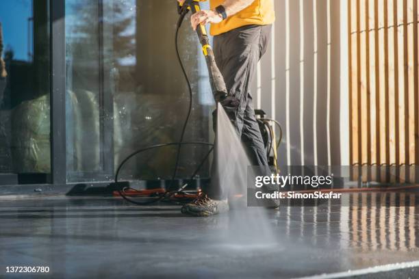 man cleaning the terrace tiles of the apartment with squirt gun - concierge stockfoto's en -beelden