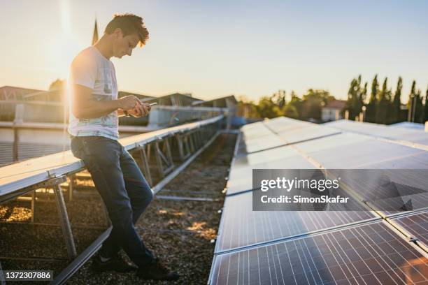 man standing beside solar energy panels using mobile phone - rooftop farm stock pictures, royalty-free photos & images