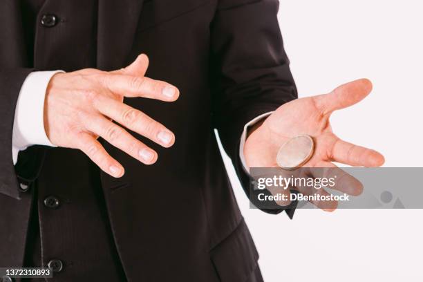 detail of the arms of a magician man dressed in a suit, making a game with a coin, on a white background. concept of magic, illusionism, luck, gambling and winning. - black jack hand stock-fotos und bilder