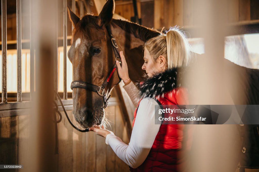 Mujer tocando y alimentando a su caballo en el rancho