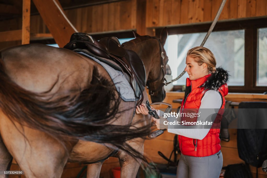 Young woman arranging stirrup on saddle