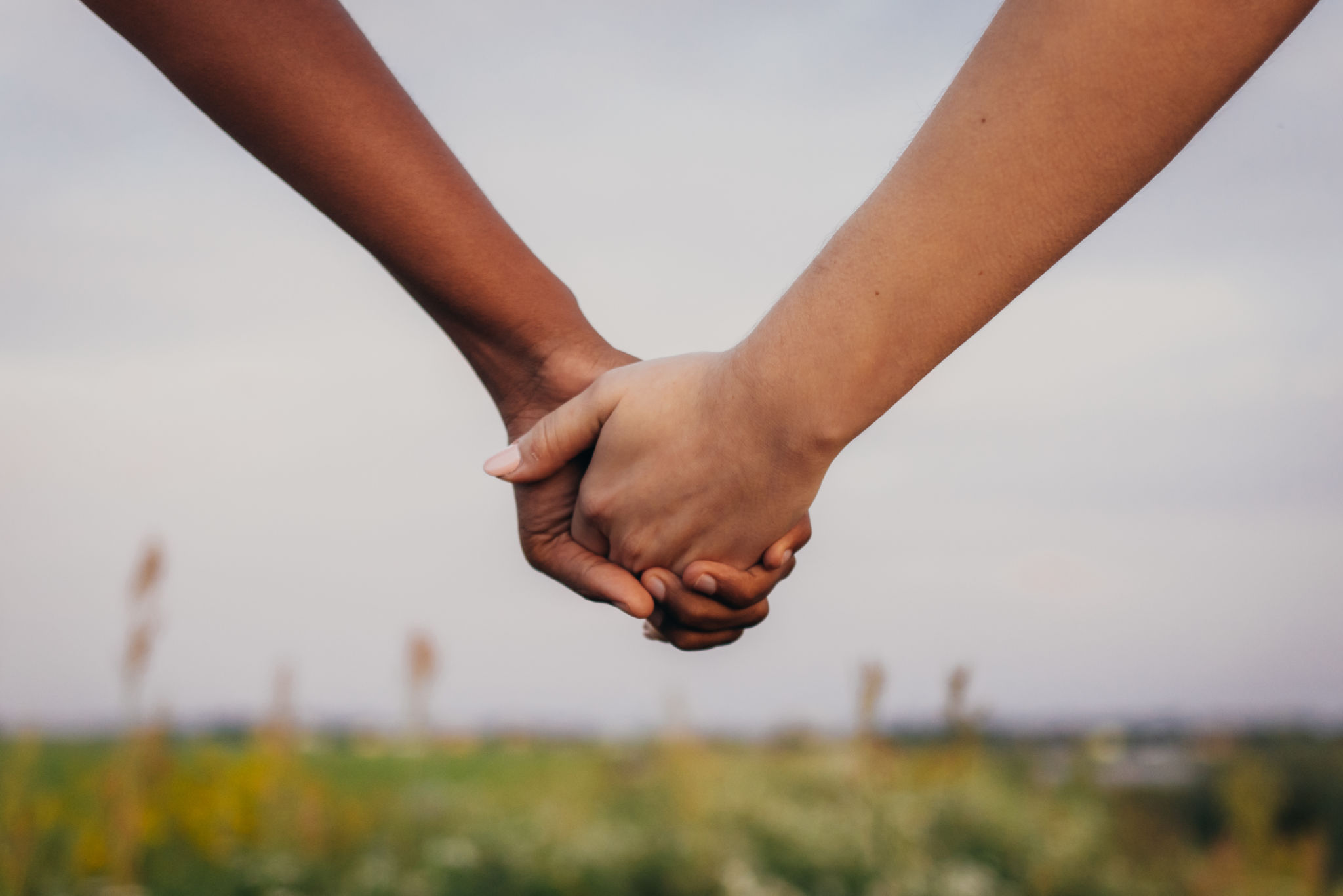 Close up of African and caucasian women holding hands on field Close up of African and caucasian women holding hands on field