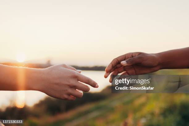 mujeres africanas y caucásicas extendiéndose las manos unas a otras - reaching fotografías e imágenes de stock