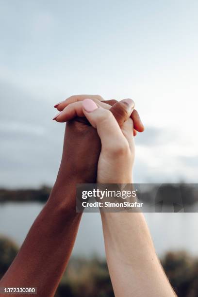 primer plano de mujeres tomadas de la mano con diferente color de piel - hands clasped fotografías e imágenes de stock