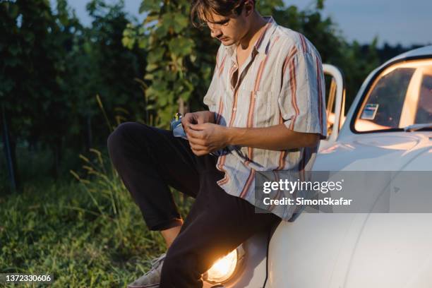 giovane che prepara la sigaretta con la carta rotolante sul cofano dell'auto nel campo - spinello foto e immagini stock