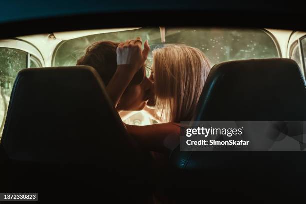 young couple kissing each other in car during date - side by side car stock pictures, royalty-free photos & images