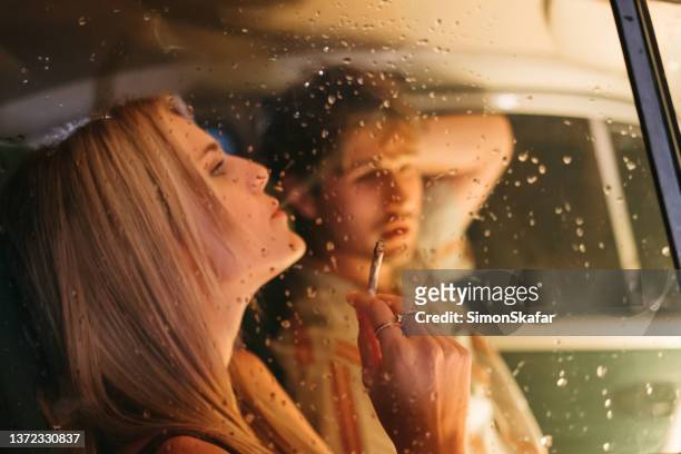 junge frau raucht marihuana-joint, während sie neben einem mann im auto sitzt - marijuana joint stock-fotos und bilder