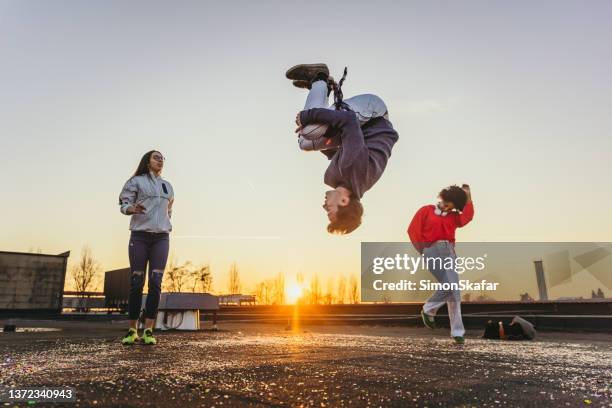 junger mann macht backflip mit frauen, die im hintergrund tanzen - akrobatik stock-fotos und bilder