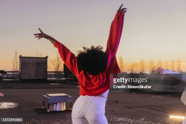 african american young woman with arms raised standing on roof against sky - head back stock pictures, royalty-free photos & images
