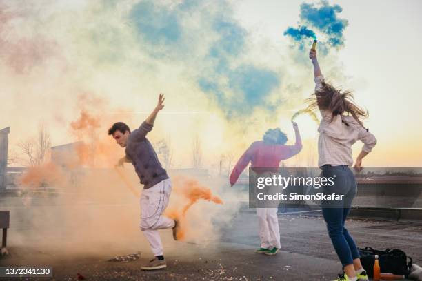 hombres y mujeres jóvenes sosteniendo bombas de humo multicolores en la azotea - de espalda fotografías e imágenes de stock