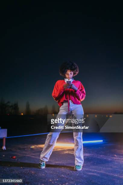 african young woman with headphones using mobile phone at night - fluorescent light 個照片及圖片檔