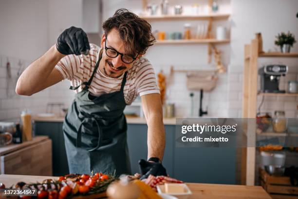 happy man sprinkling pepper on steak in kitchen - sprinkling imagens e fotografias de stock