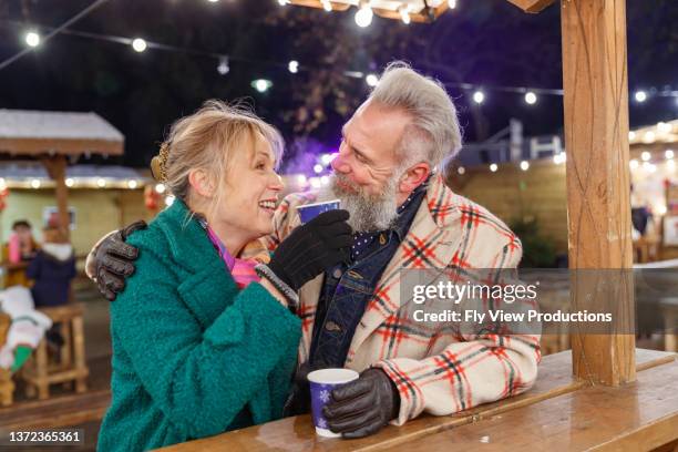 glückliches rentnerpaar, das heiße getränke beim winterstraßenfest im freien genießt - boomer couple out on town stock-fotos und bilder