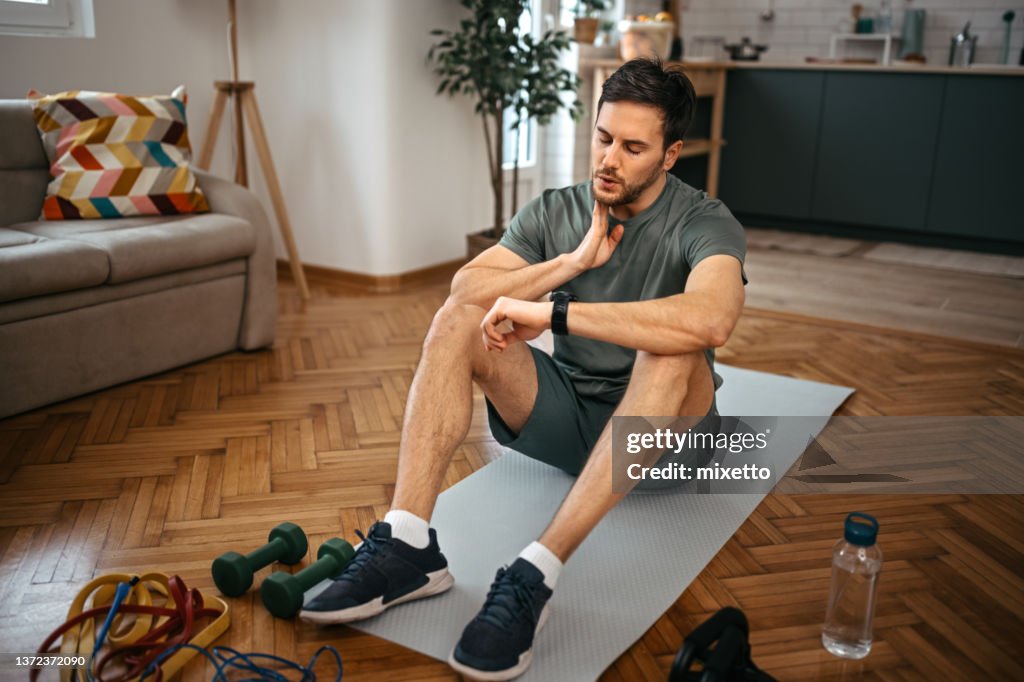 Man looking at fitness tracker while sitting on mat at home