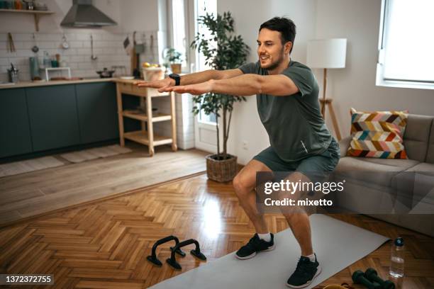 smiling man practicing squats at home - agachar se imagens e fotografias de stock